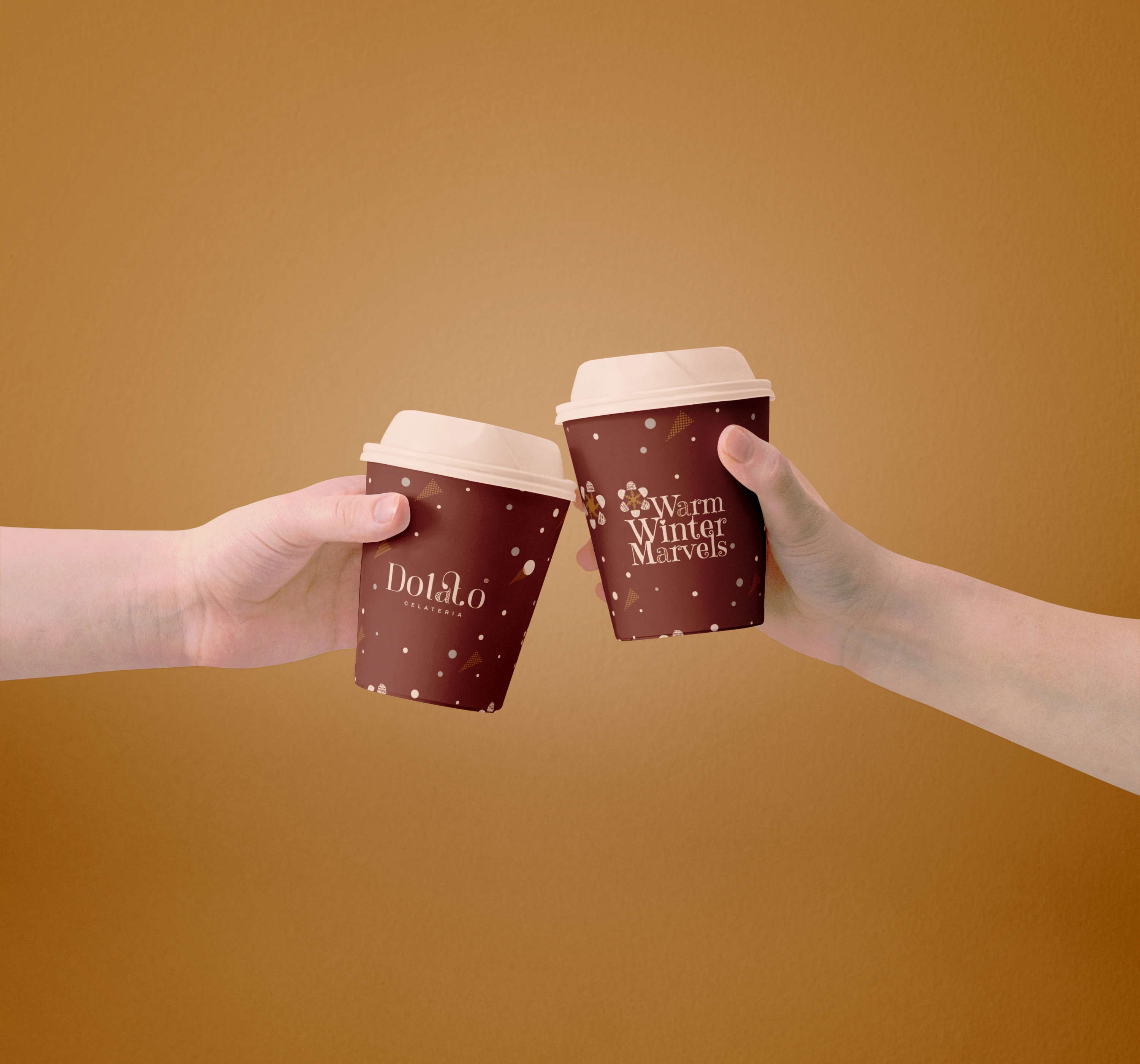 Two hands holding burgundy Dolato hot chocolate cups featuring the Warm Winter Marvels winter pattern.